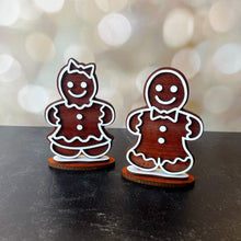 Load image into Gallery viewer, Two wooden gingerbread man figurines on a dark surface with a blurred bokeh background.