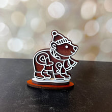 Load image into Gallery viewer, Wooden figurine of a bear wearing a hat and scarf on a dark surface with a blurred light background