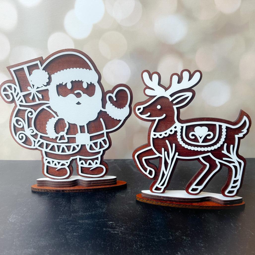 Wooden Christmas decorations of Santa Claus and a reindeer on a dark surface with a blurred light background.