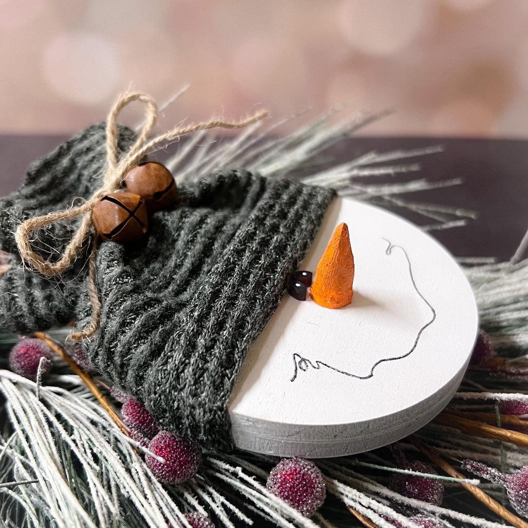 Decorative heart-shaped ornament with a face, surrounded by winter elements.