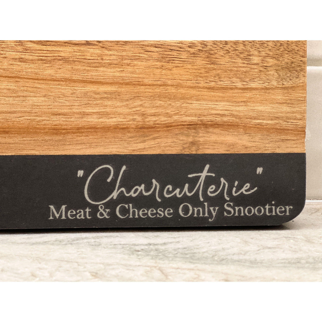 Wooden charcuterie board with engraved phrase “Charcuterie Meat & Cheese Only Snootier,” displayed on a marble countertop.