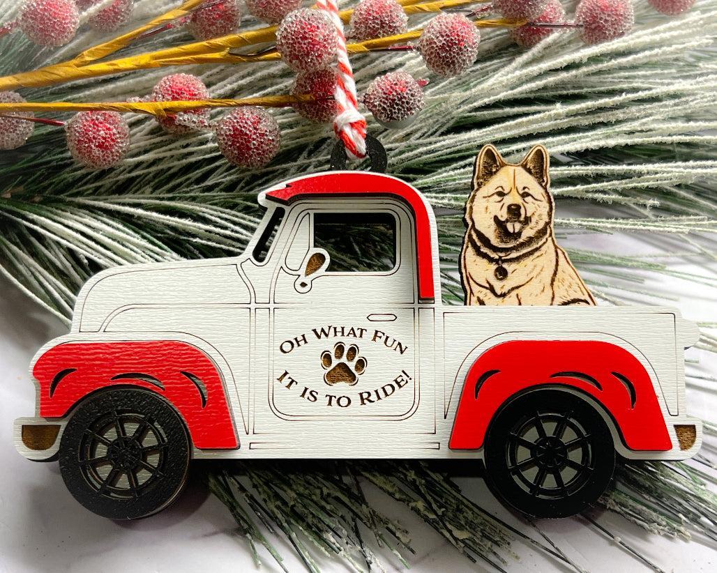 A vintage style red and white truck ornament with a dog riding in the back seat, placed on a branch with Christmas decorations.