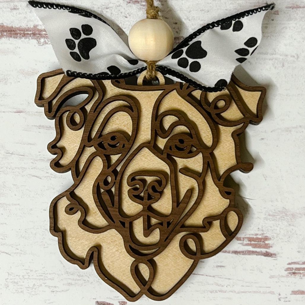 Laser-cut wooden doodle art dog ornament with paw print ribbon bow and bead, hanging on rustic twine.