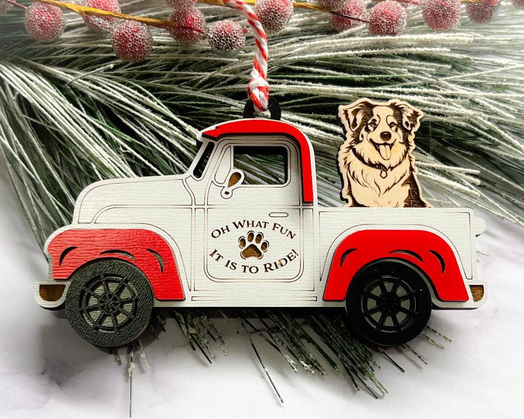 A vintage style red and white truck ornament with a dog riding in the back seat, placed on a branch with Christmas decorations.
