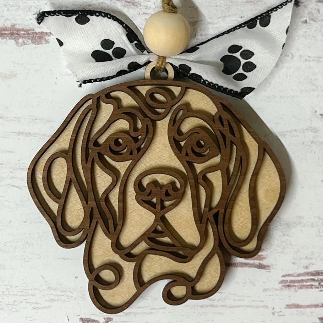 Laser-cut wooden doodle art dog ornament with paw print ribbon bow and bead, hanging on rustic twine.