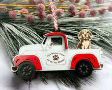 Load image into Gallery viewer, A vintage style red and white truck ornament with a dog riding in the back seat, placed on a branch with Christmas decorations.