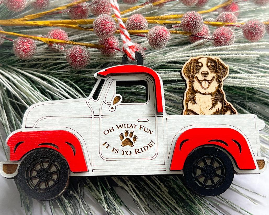 A vintage style red and white truck ornament with a dog riding in the back seat, placed on a branch with Christmas decorations.