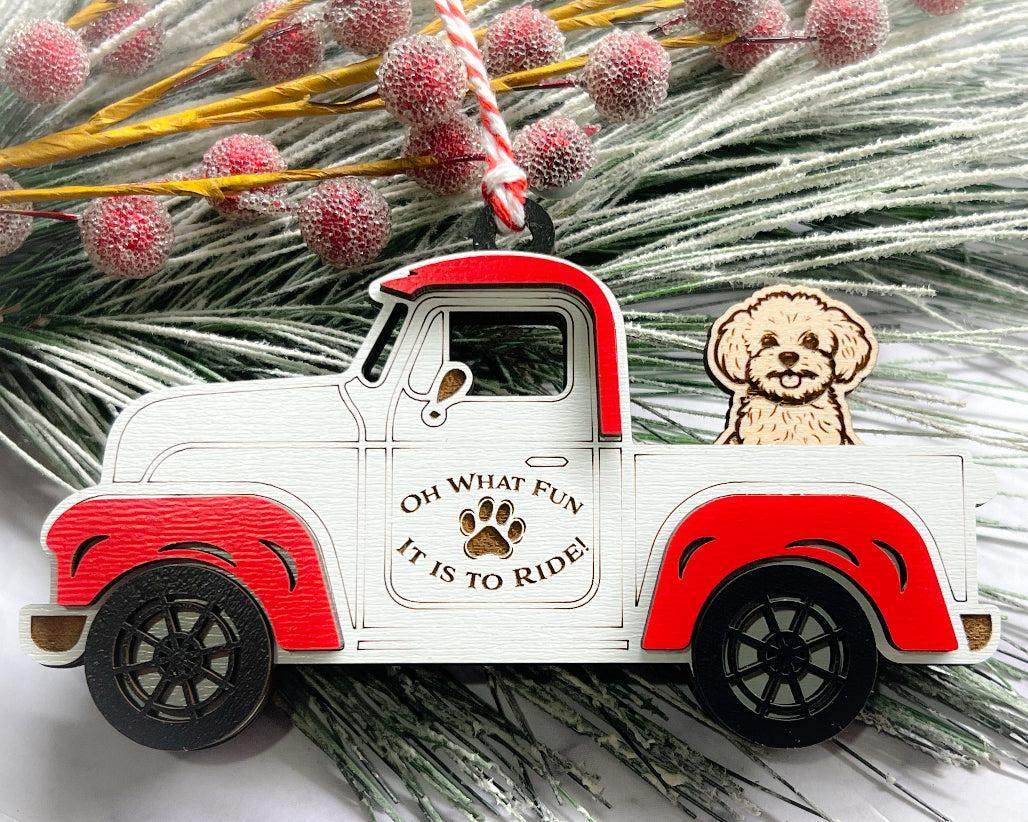 A vintage style red and white truck ornament with a dog riding in the back seat, placed on a branch with Christmas decorations.