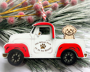 A vintage style red and white truck ornament with a dog riding in the back seat, placed on a branch with Christmas decorations.
