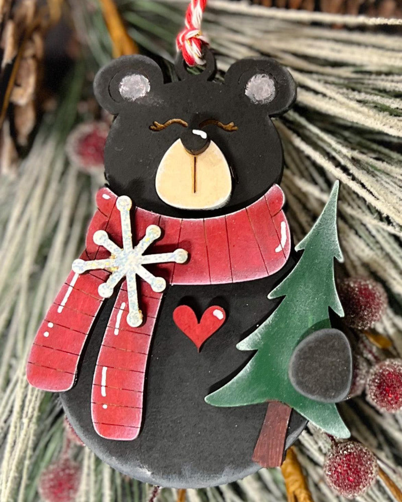 Decorative bear ornament with a red scarf, snowflake, heart, and tree on a natural background.