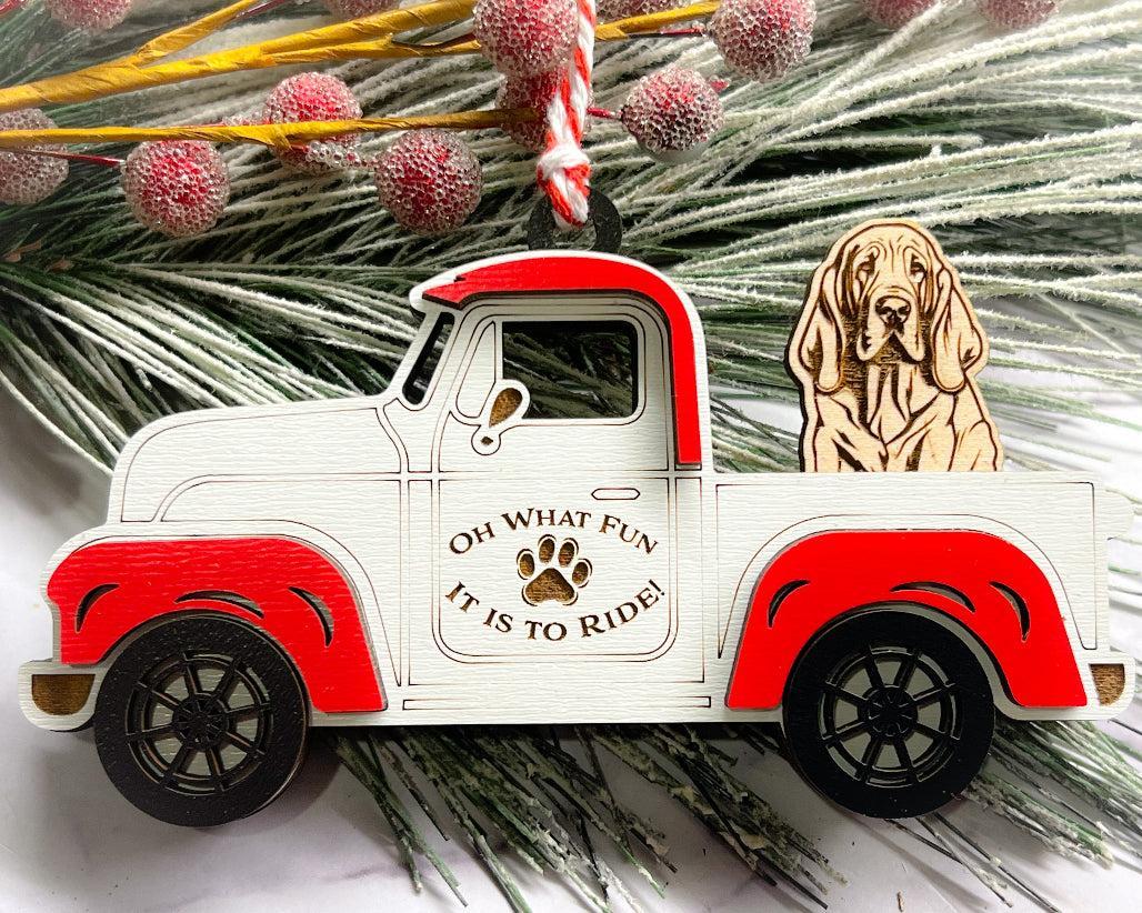 A vintage style red and white truck ornament with a dog riding in the back seat, placed on a branch with Christmas decorations.