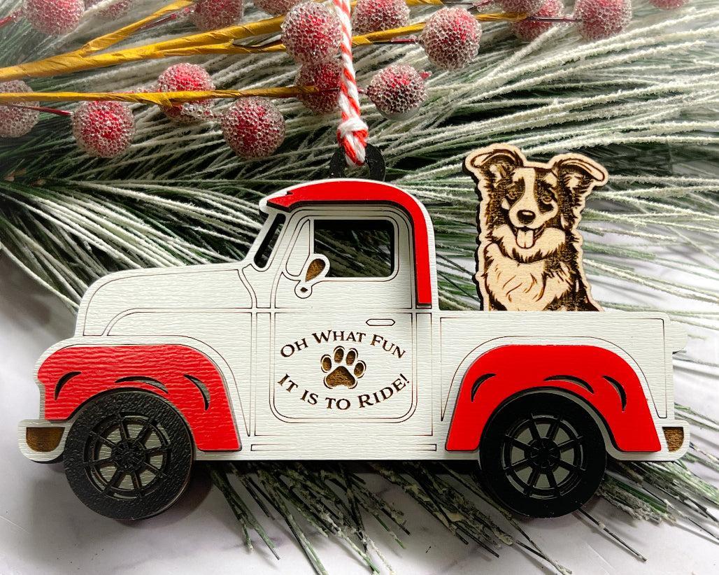 A vintage style red and white truck ornament with a dog riding in the back seat, placed on a branch with Christmas decorations.