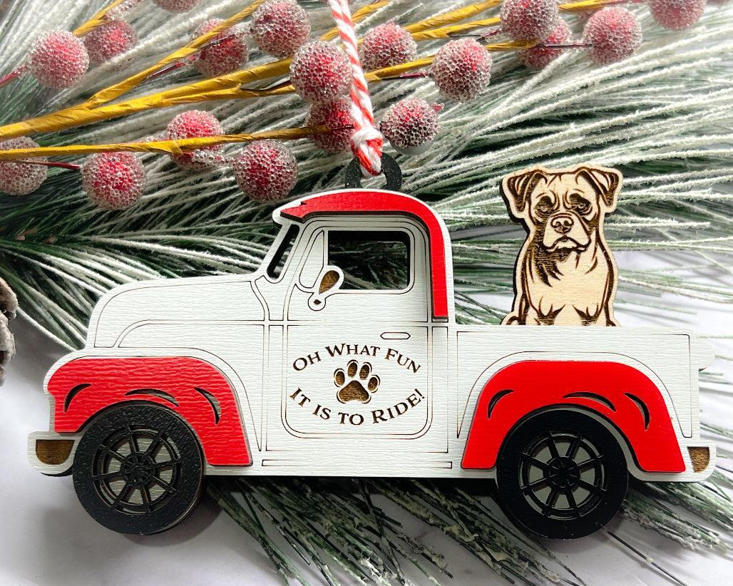 A vintage style red and white truck ornament with a dog riding in the back seat, placed on a branch with Christmas decorations.