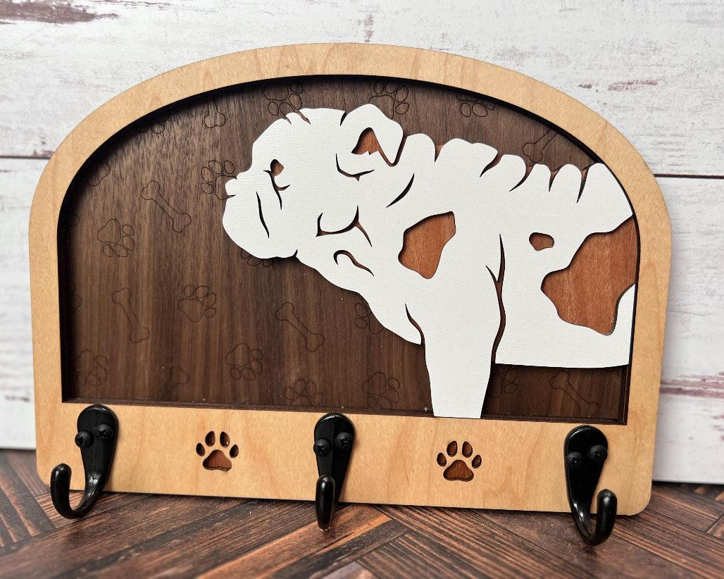 A wooden dog leash holder with a cut-out silhouette of a dog and the phrase 'Unleash Adventure'. It features three hooks at the bottom and paw prints around the dog's silhouette.