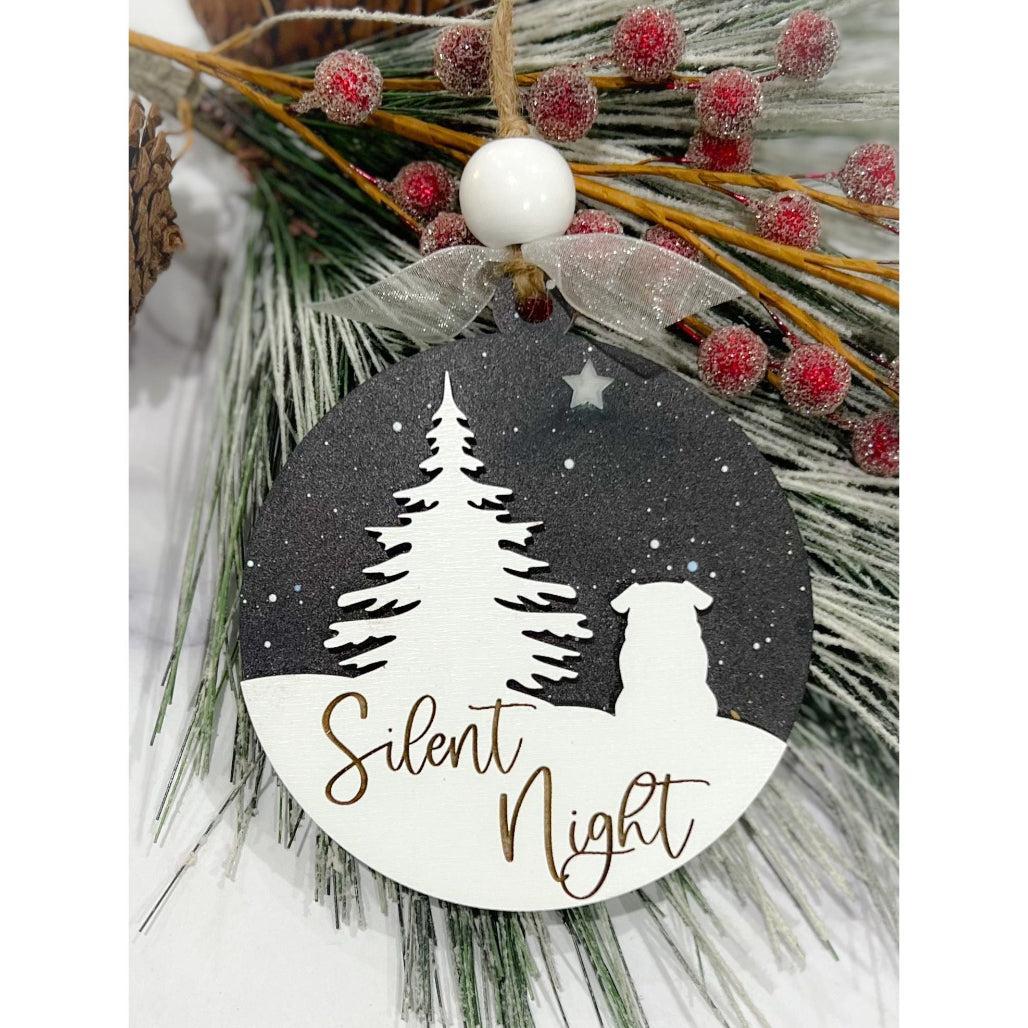 A round ornament with a silhouette of a bulldog and the text 'Silent Night' on it, against a night sky with stars, attached to a Christmas tree branch with red berries.