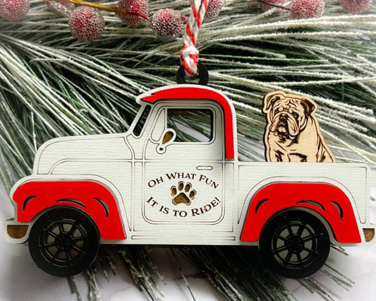 A vintage style red and white truck ornament with a dog riding in the back seat, placed on a branch with Christmas decorations.
