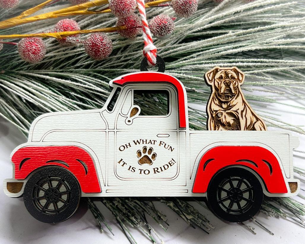 A vintage style red and white truck ornament with a dog riding in the back seat, placed on a branch with Christmas decorations.