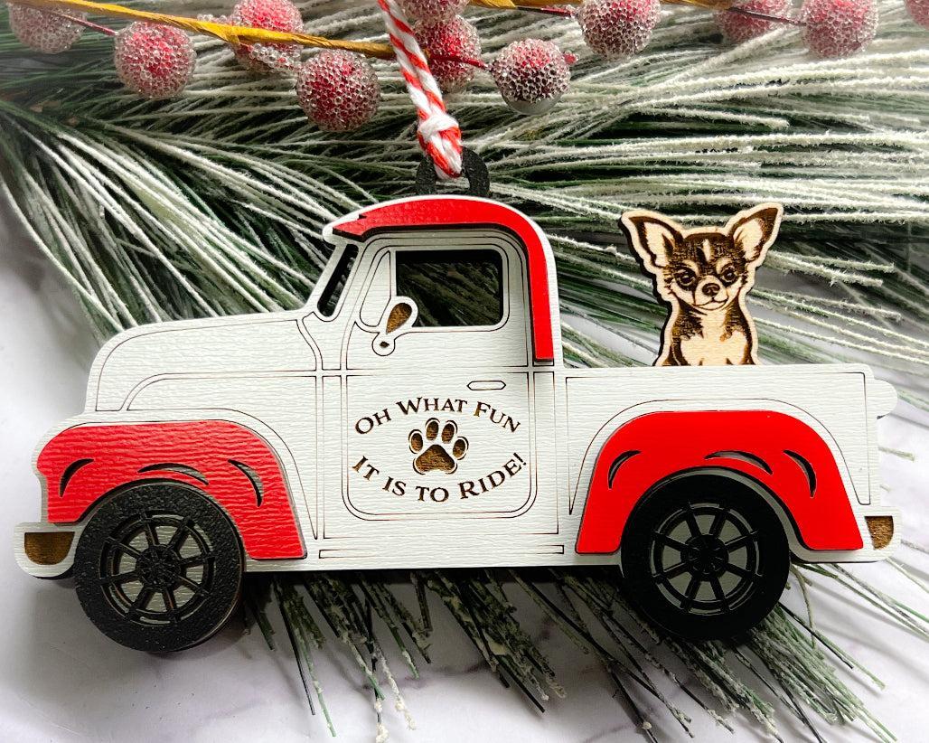 A vintage style red and white truck ornament with a dog riding in the back seat, placed on a branch with Christmas decorations.
