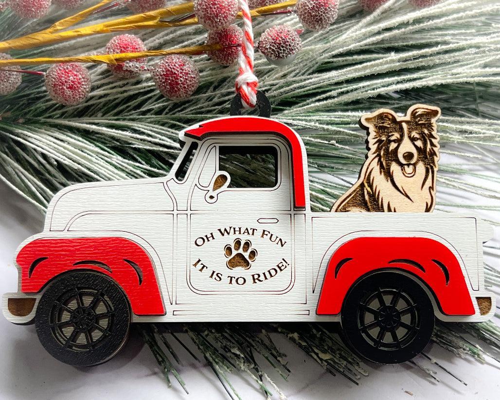 A vintage style red and white truck ornament with a dog riding in the back seat, placed on a branch with Christmas decorations.