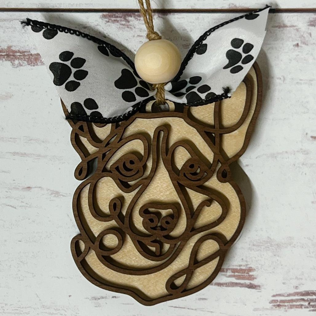 Laser-cut wooden doodle art dog ornament with paw print ribbon bow and bead, hanging on rustic twine.