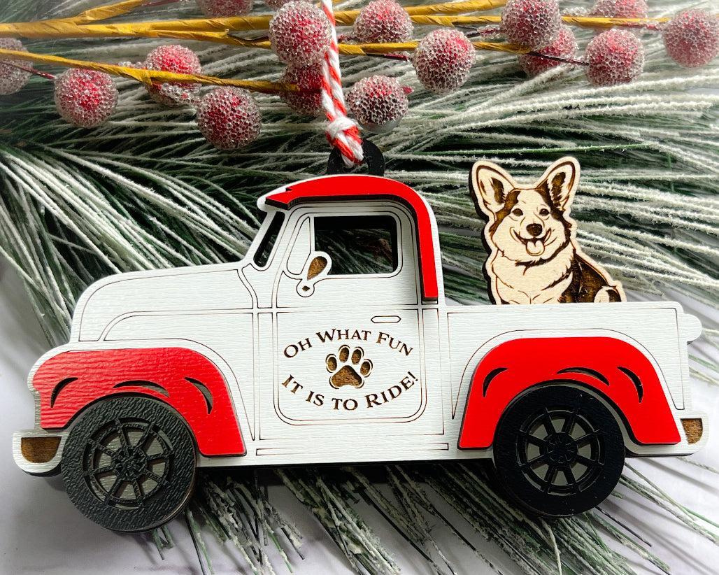 A vintage style red and white truck ornament with a dog riding in the back seat, placed on a branch with Christmas decorations.