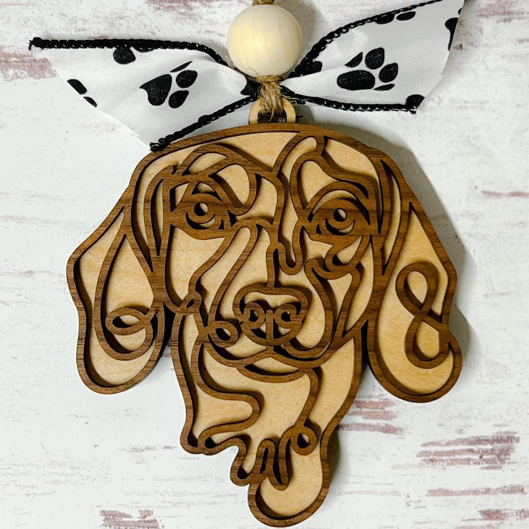 Laser-cut wooden doodle art dog ornament with paw print ribbon bow and bead, hanging on rustic twine.
