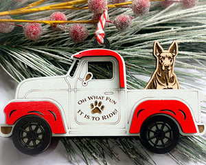 A vintage style red and white truck ornament with a dog riding in the back seat, placed on a branch with Christmas decorations.