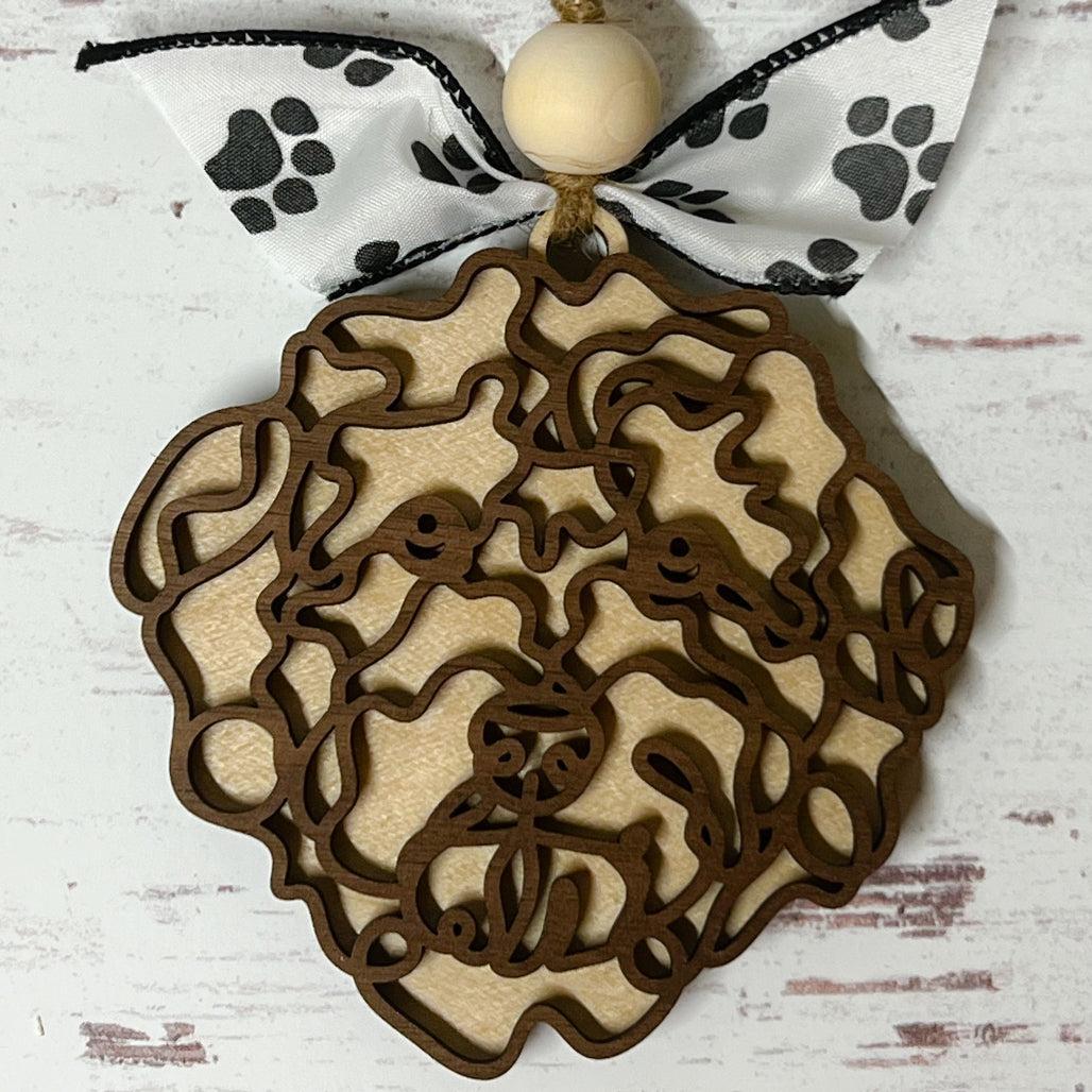 Laser-cut wooden doodle art dog ornament with paw print ribbon bow and bead, hanging on rustic twine.