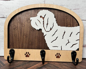 A wooden dog leash holder with a cut-out silhouette of a dog and the phrase 'Unleash Adventure'. It features three hooks at the bottom and paw prints around the dog's silhouette.