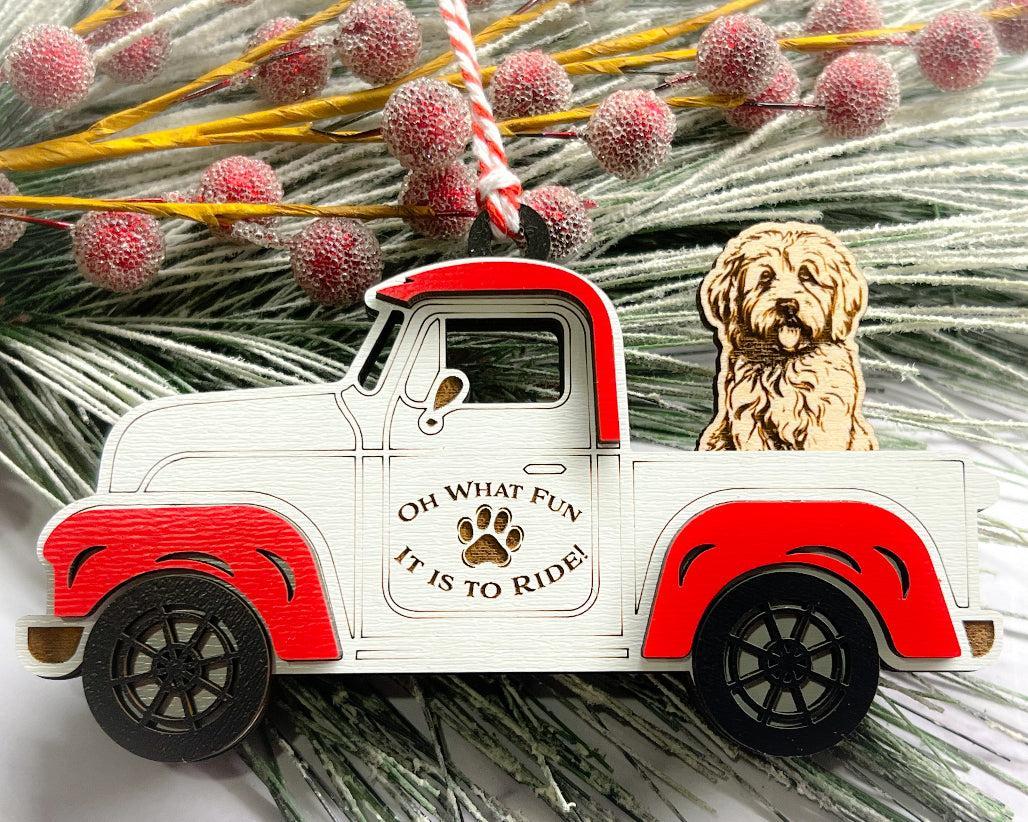A vintage style red and white truck ornament with a dog riding in the back seat, placed on a branch with Christmas decorations.