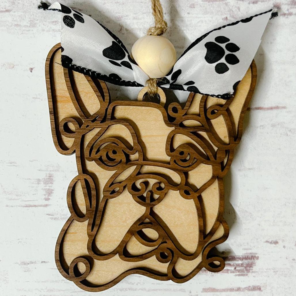 Laser-cut wooden doodle art dog ornament with paw print ribbon bow and bead, hanging on rustic twine.
