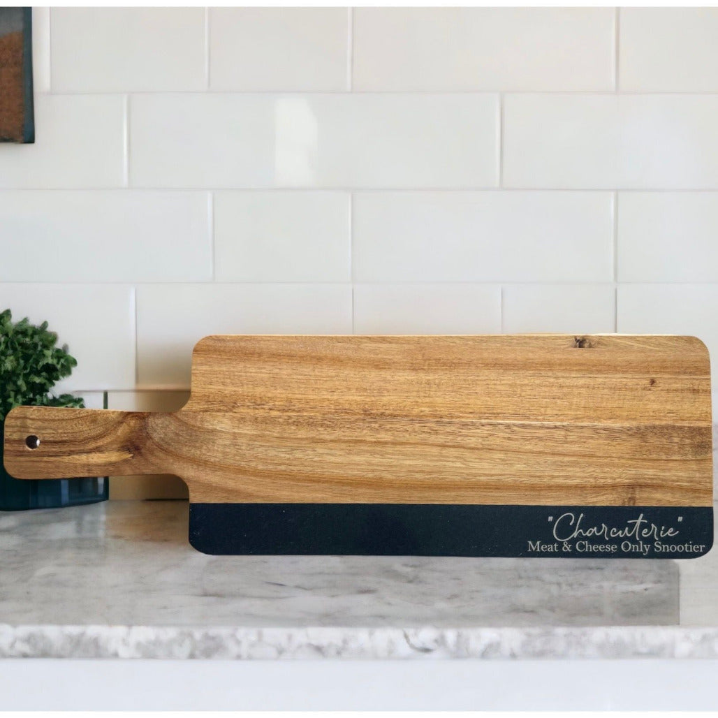 Wooden charcuterie board with engraved phrase “Charcuterie Meat & Cheese Only Snootier,” displayed on a marble countertop.