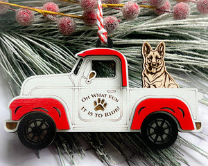 A vintage style red and white truck ornament with a dog riding in the back seat, placed on a branch with Christmas decorations.