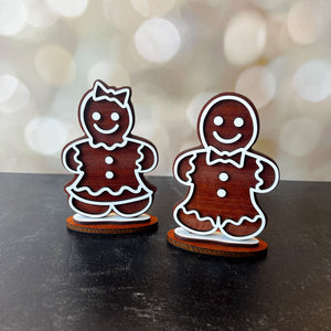 Two wooden gingerbread man figurines on a dark surface with a blurred bokeh background.
