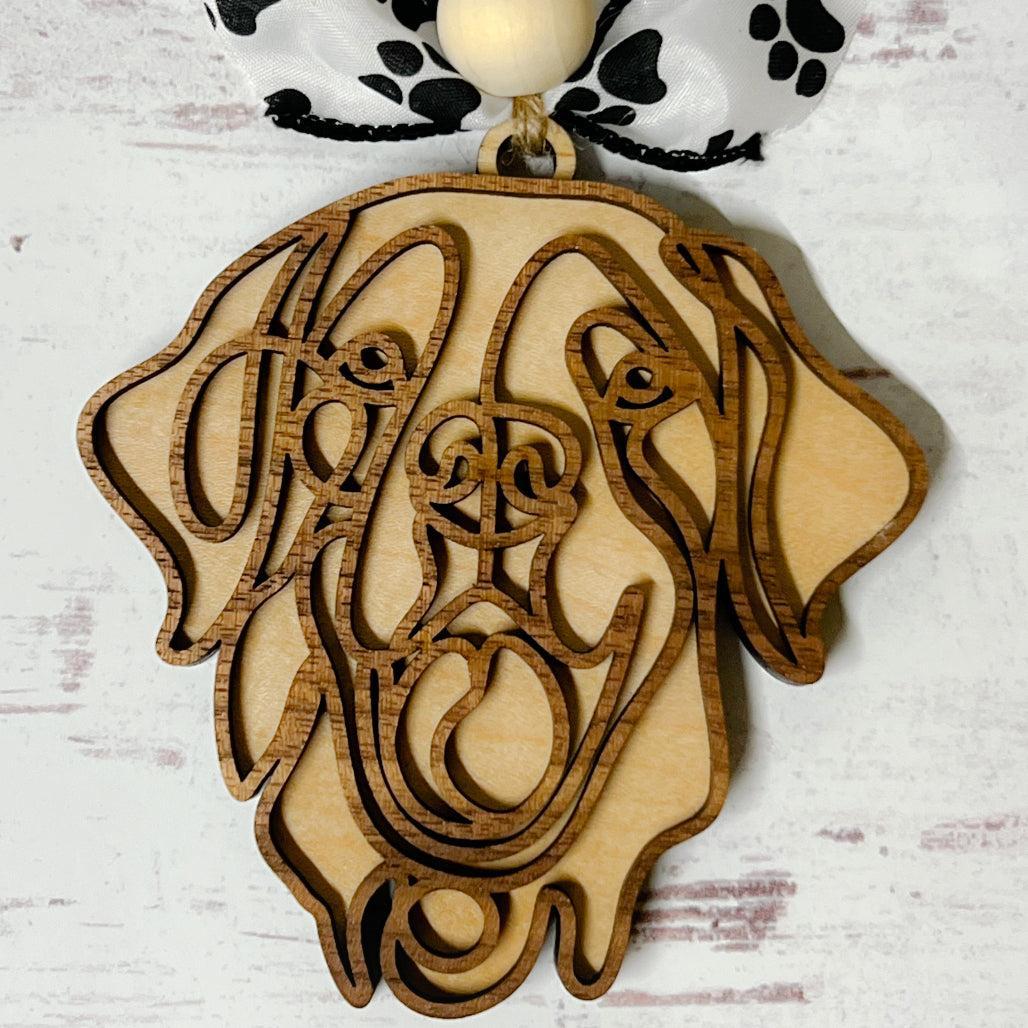 Laser-cut wooden doodle art dog ornament with paw print ribbon bow and bead, hanging on rustic twine.