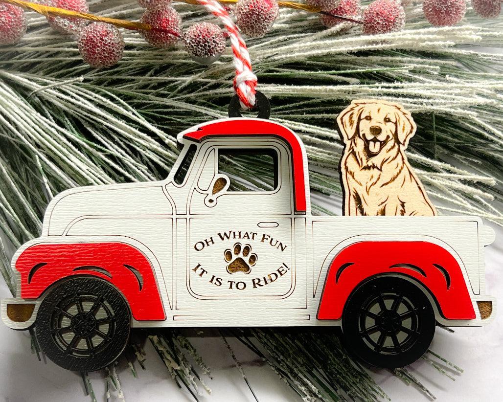 A vintage style red and white truck ornament with a dog riding in the back seat, placed on a branch with Christmas decorations.