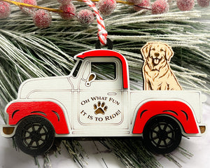 A vintage style red and white truck ornament with a dog riding in the back seat, placed on a branch with Christmas decorations.