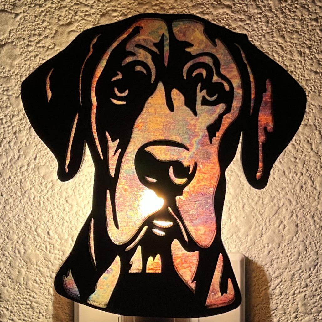 A laser-cut wooden night light in the shape of a dog's head, glowing with a warm light.