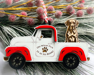A vintage style red and white truck ornament with a dog riding in the back seat, placed on a branch with Christmas decorations.