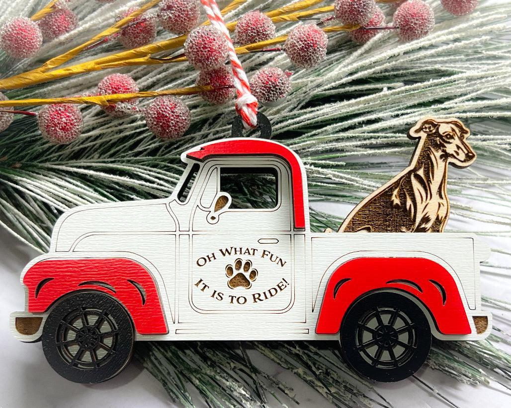A vintage style red and white truck ornament with a dog riding in the back seat, placed on a branch with Christmas decorations.