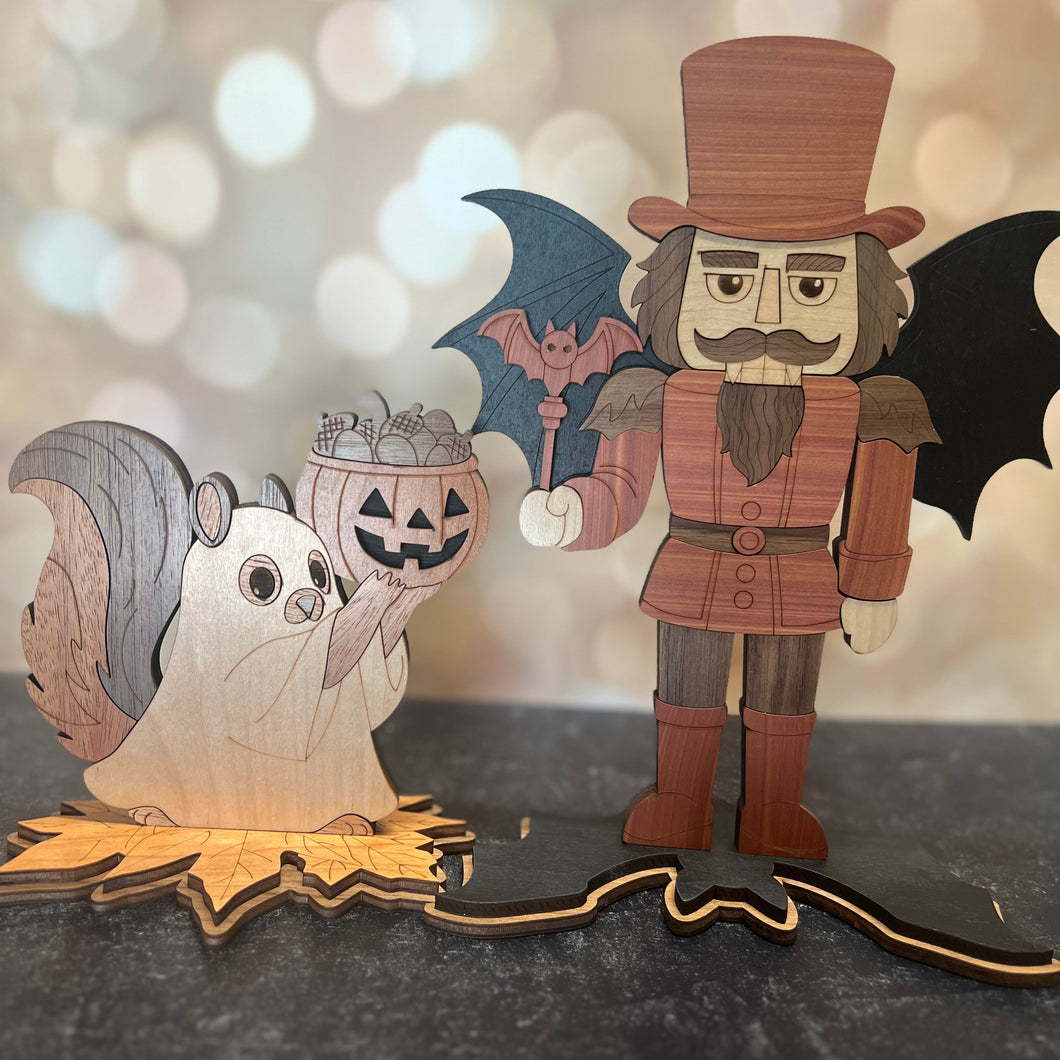 Wooden Halloween decorations including a ghost, pumpkin, bat, and witch on a dark surface with a blurred light background.