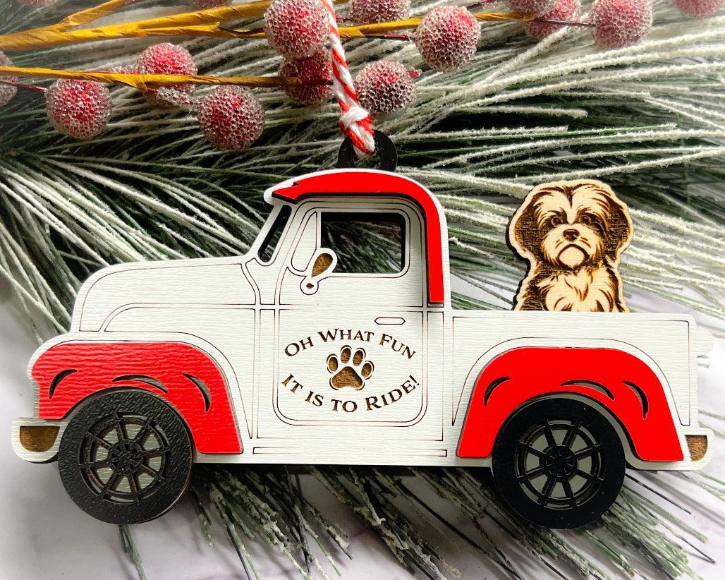 A vintage style red and white truck ornament with a dog riding in the back seat, placed on a branch with Christmas decorations.