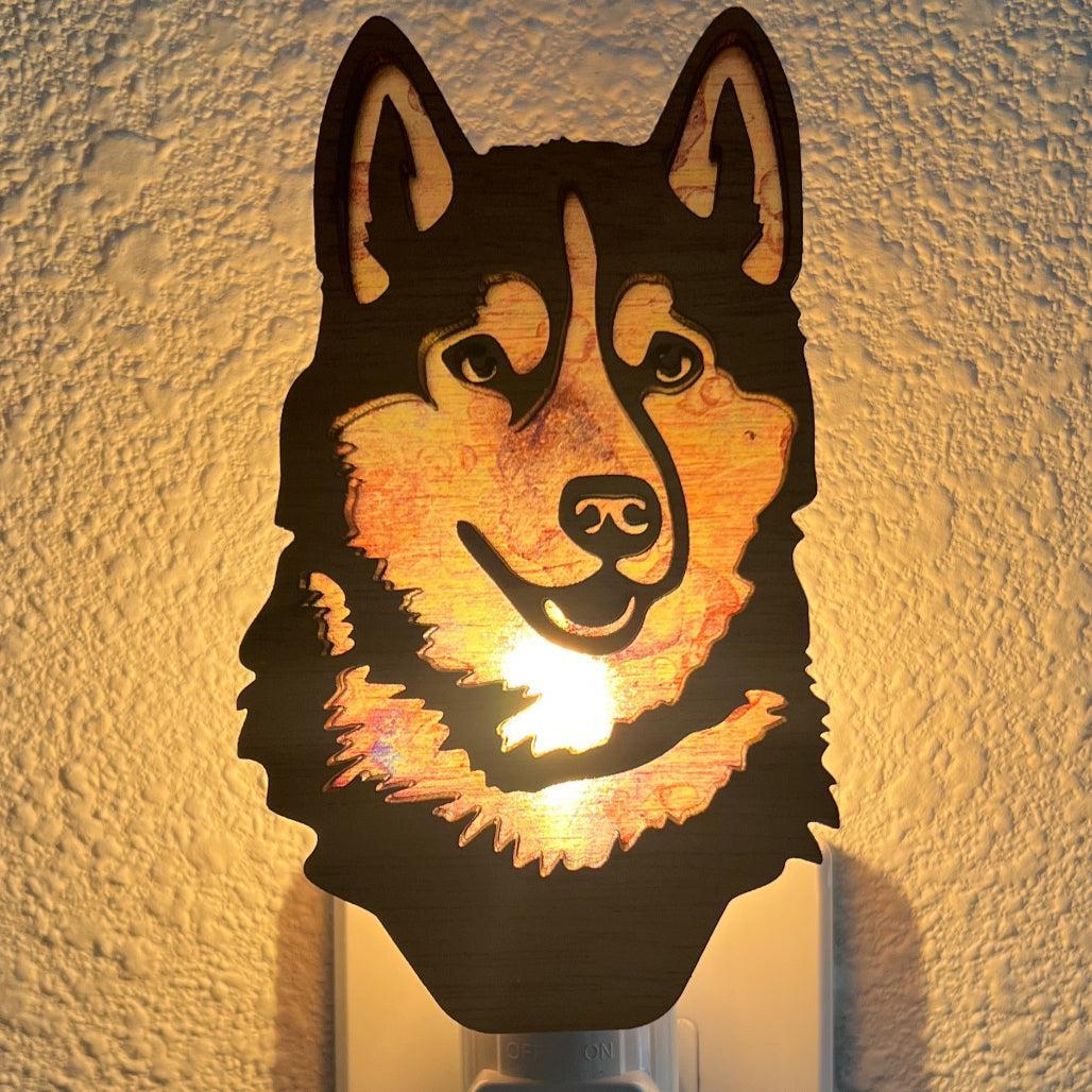 A laser-cut wooden night light in the shape of a dog's head, glowing with a warm light.