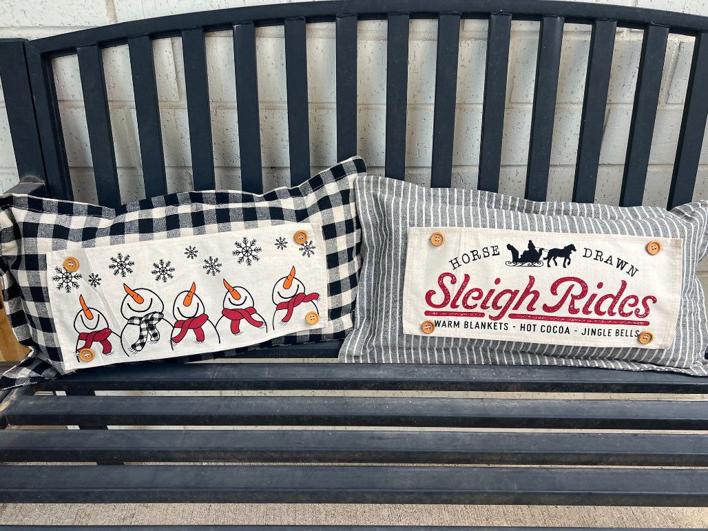 Two decorative pillows on a bench with festive designs and text.
