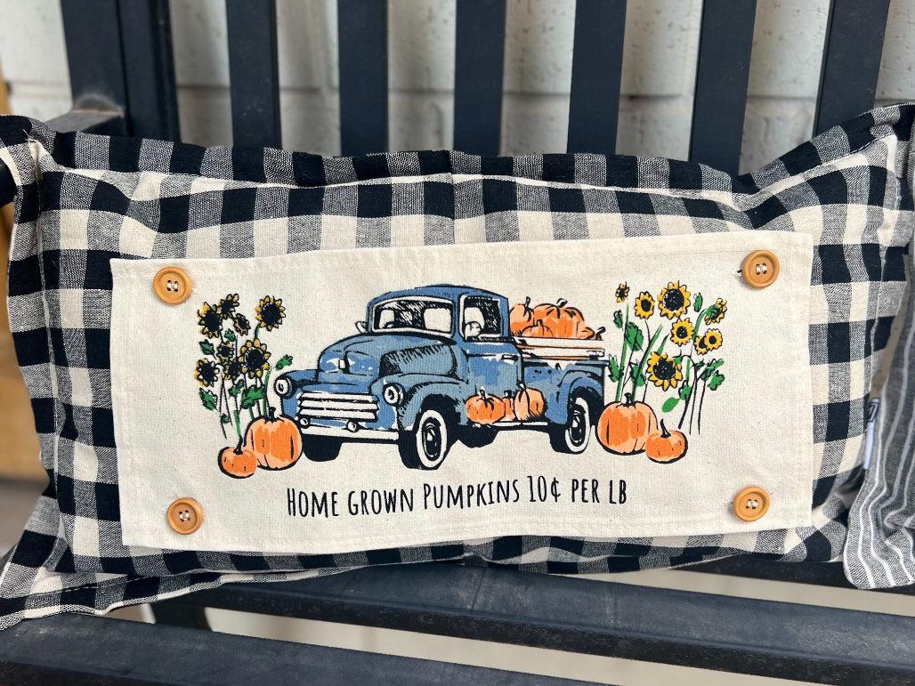 Decorative pillow with a blue truck and pumpkins design on a black and white checkered background.