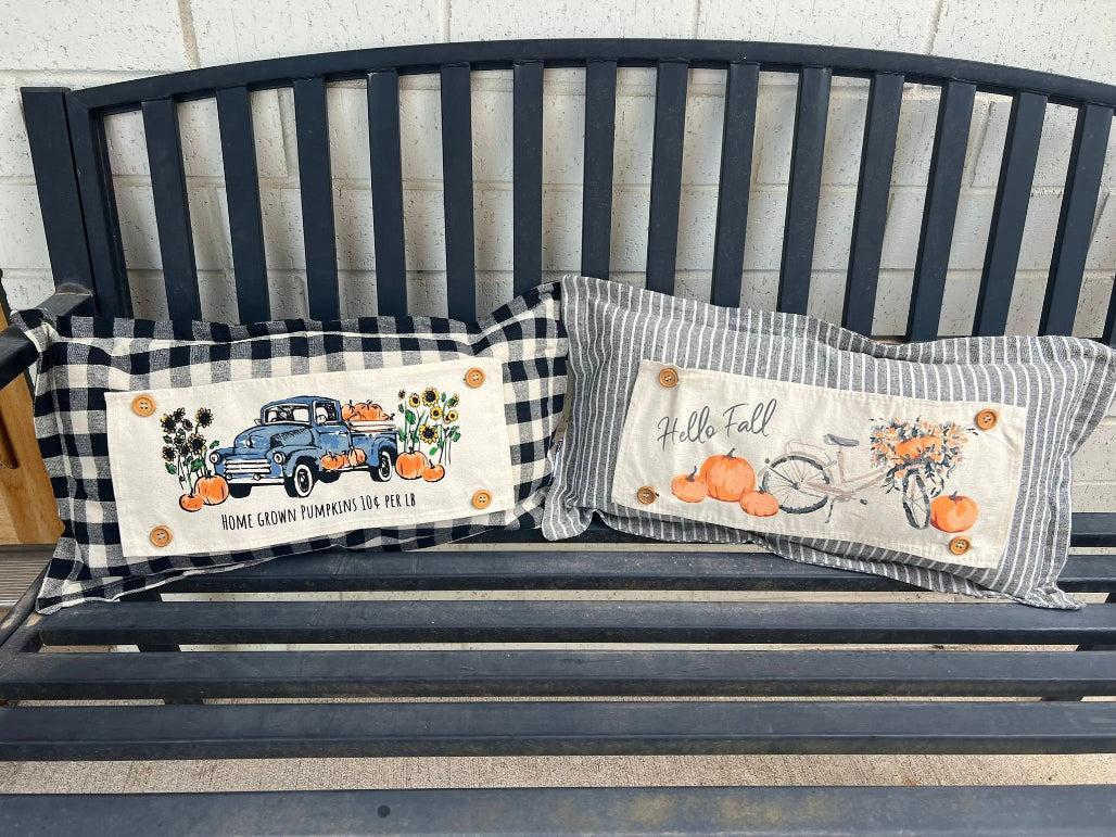 Two decorative pillows with autumn-themed designs on a black bench.