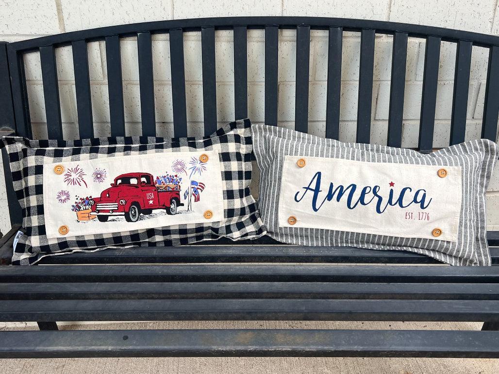 Two decorative pillows on a bench with one featuring a red truck and the other displaying 'America'.