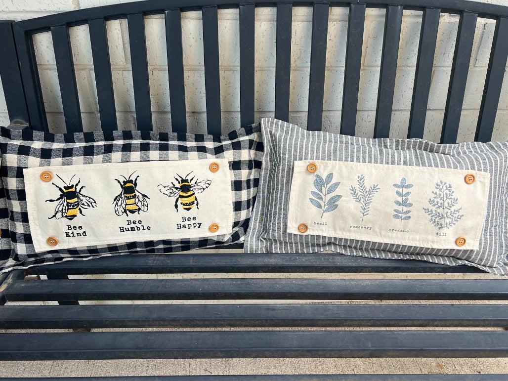 Two decorative pillows with bee-themed designs on a bench.