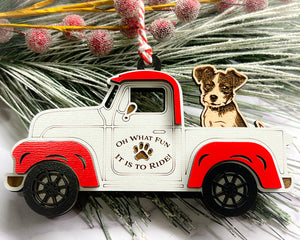 A vintage style red and white truck ornament with a dog riding in the back seat, placed on a branch with Christmas decorations.