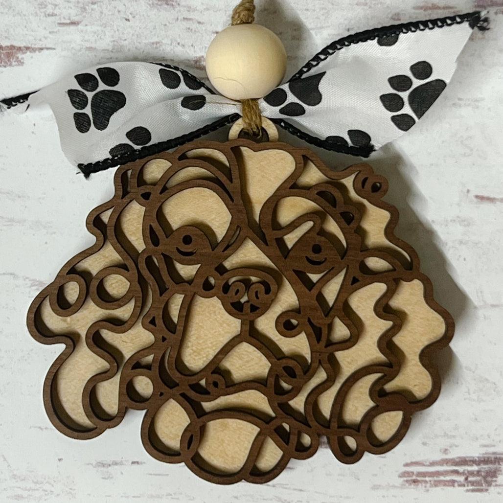 Laser-cut wooden doodle art dog ornament with paw print ribbon bow and bead, hanging on rustic twine.